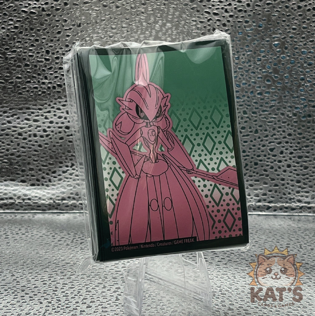 A sealed trading card sleeve featuring an illustration of a pink armored fantasy character against a green patterned background, photographed on a clear stand against a textured metallic backdrop.